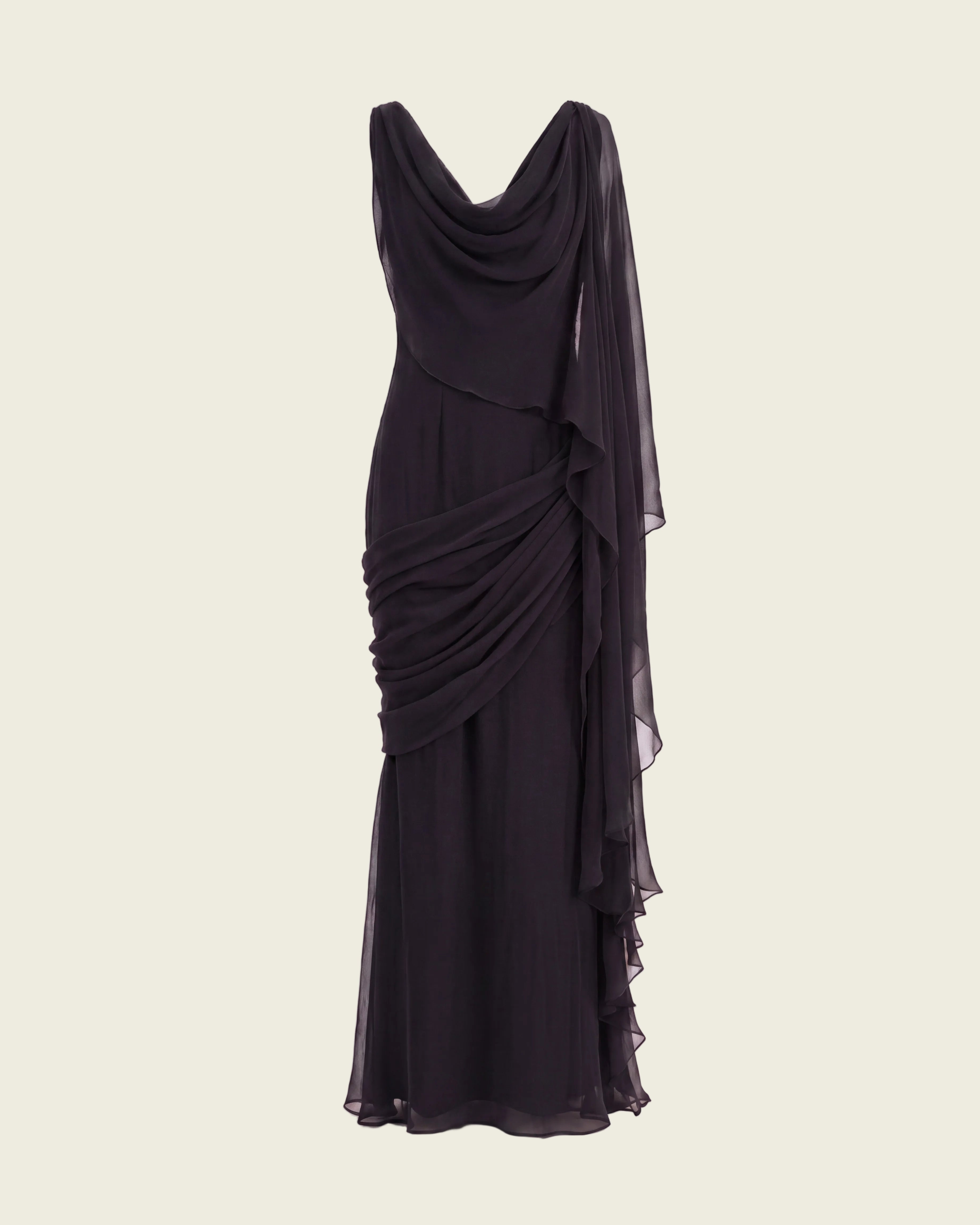 A floor-length black draped gown with a deep V-neckline, layered ruffle details, and a sheer flowing overlay, displayed against a plain white studio background.
