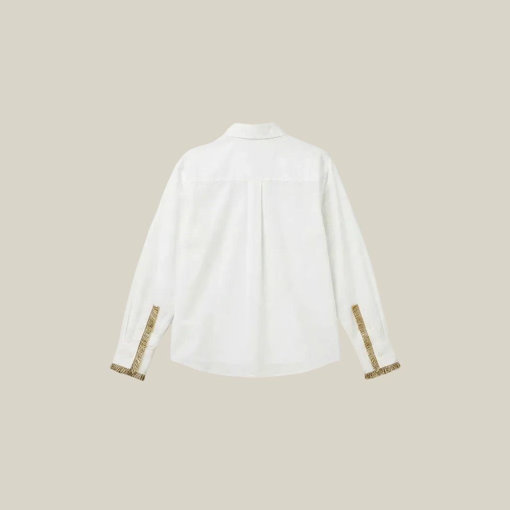 White shirt with gold trim on cuffs and collar against a beige background