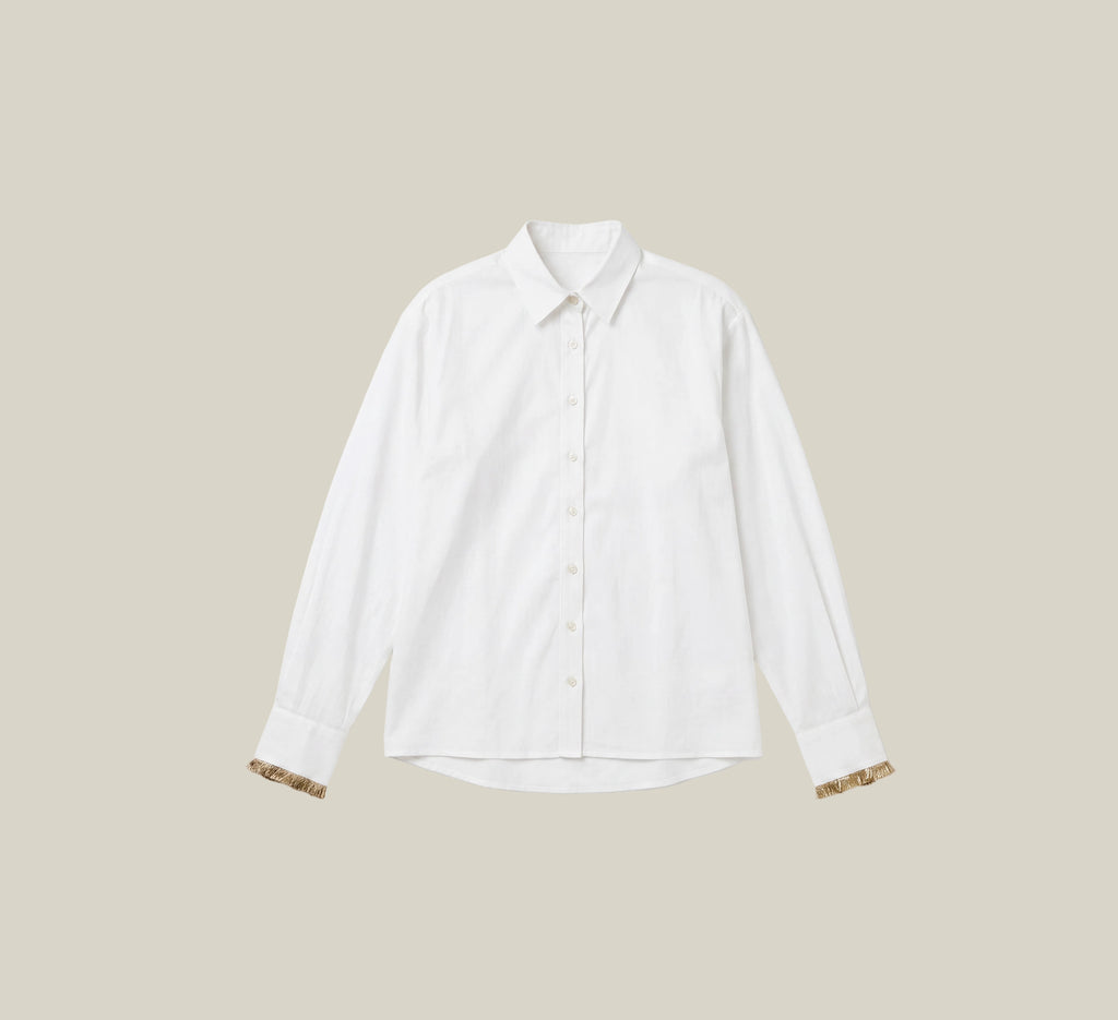 A white long-sleeve button-up shirt with patterned cufflinks, displayed flat against a light cream background.